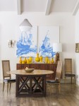 Wood dining table and chairs in light dinging area with hardwood floor, bowl with large grapes, wall hutch with various sized yellow ceramics, lamp, and wall painting.