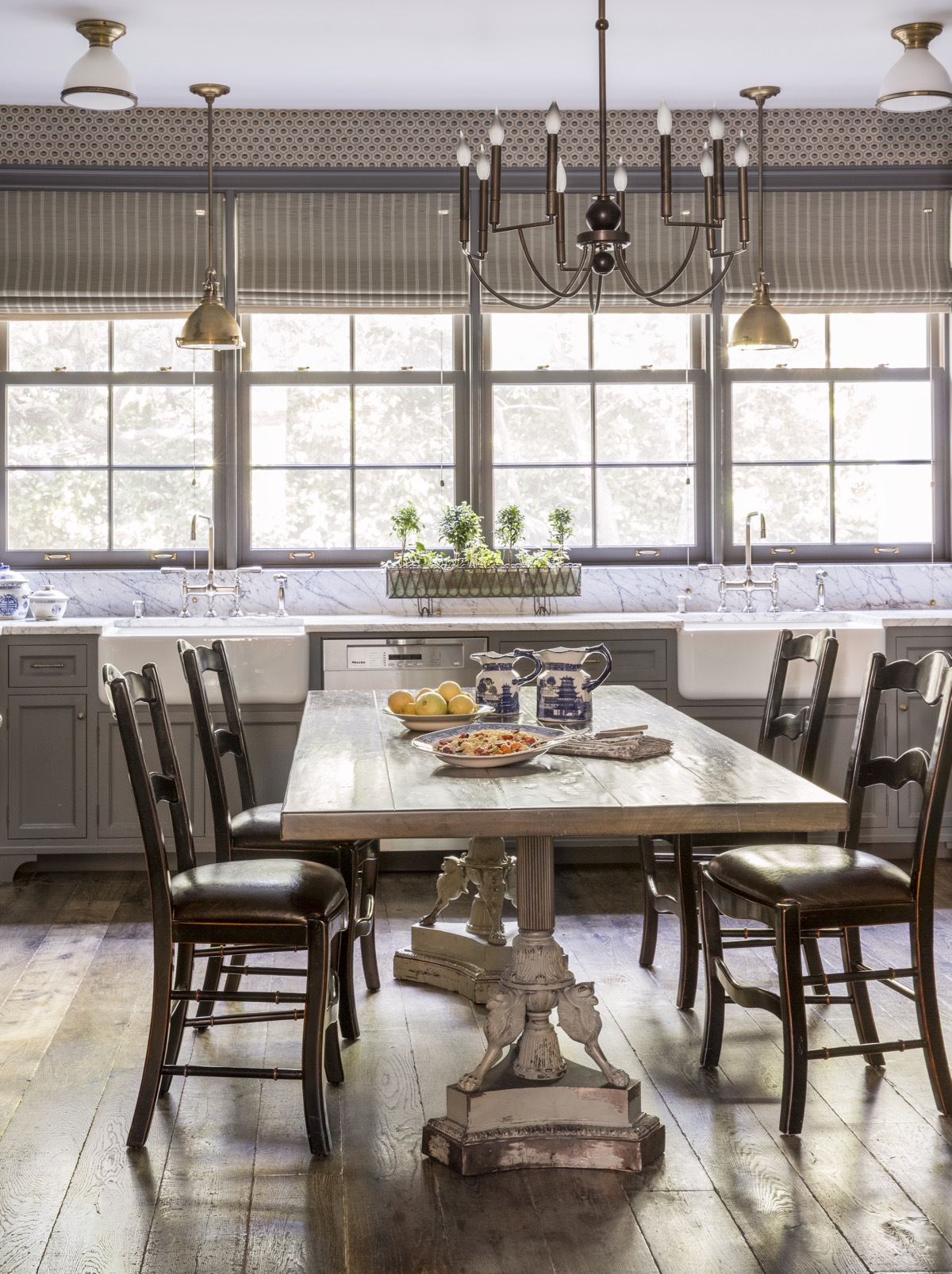 Lage kitchen with wood dining table, hardwood floors, stone countertops, and large windows looking out to green yard..