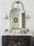 Detail of bathroom vanity with antique finish, stone top, various containers, flowers on countertop.