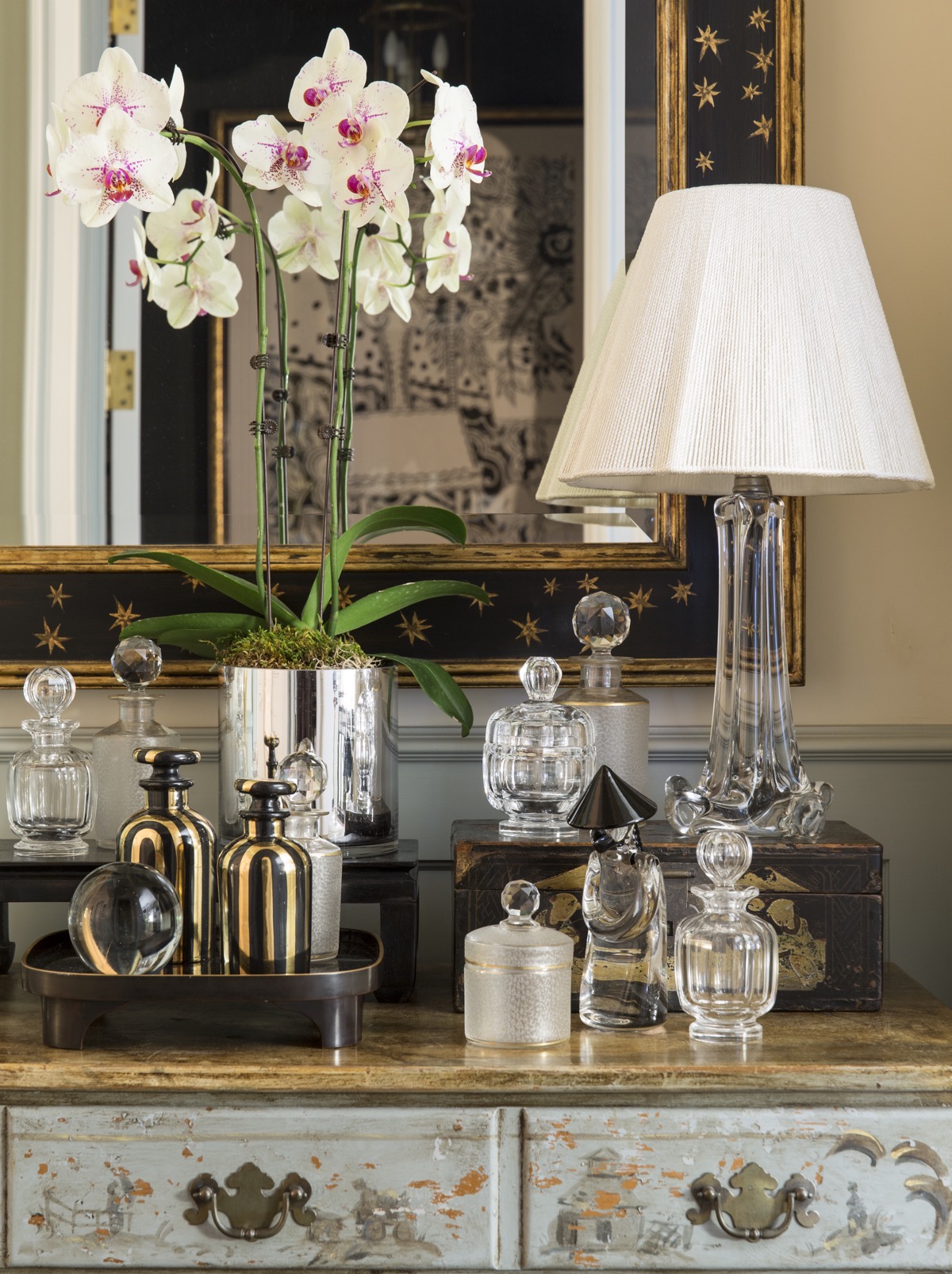 Antique perfume bottles sitting on top dresser with lamp in front of mirrow